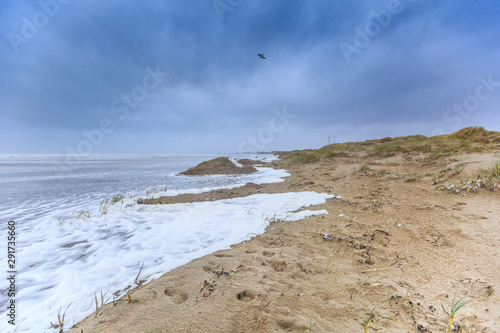 Severe storm along Dutch North Sea coast put Beach to the dunes under water against a background with dark clouds and foaming sea