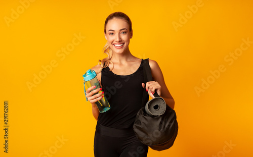 Positive Sporty Girl Holding Bag, Mat And Water, Yellow Background
