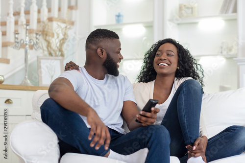 Cheerful couple sitting on couch watching funny videos on tv