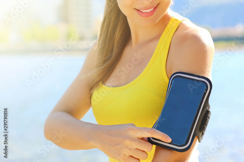 Sport armband for smartphone. Sporty girl touching her smart phone before outdoor fitness workout at the beach.