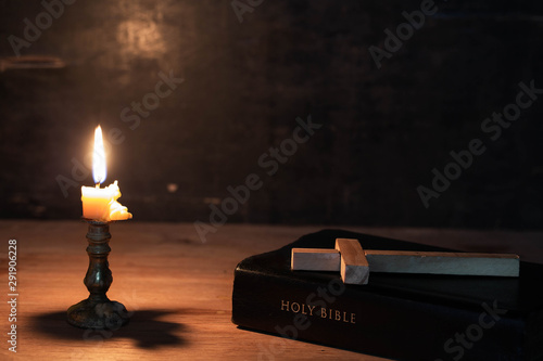 Wood cross laying on an Bible, with candle and candlelight on table