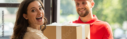 panoramic shot of happy woman receiving carton box from cheerful delivery man