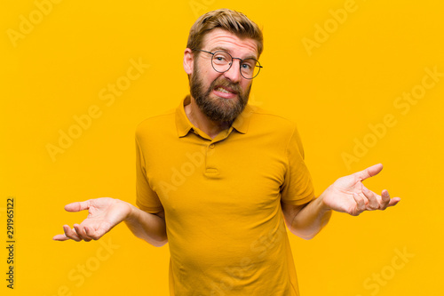 young blonde man feeling clueless and confused, not sure which choice or option to pick, wondering against orange wall