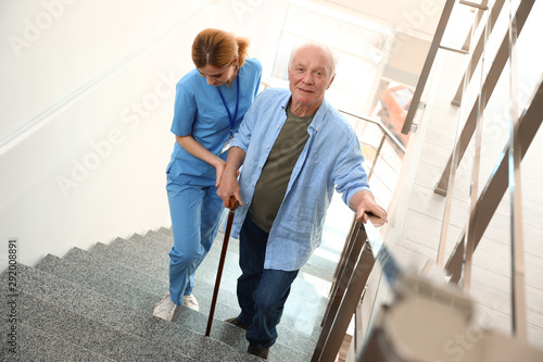 Nurse assisting elderly man on stairs indoors