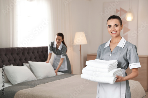 Chambermaid with stack of fresh towels in hotel room. Space for text