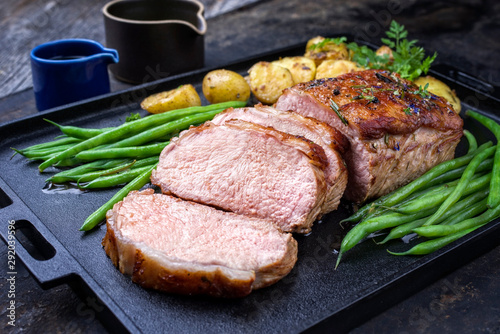 Traditional roasted dry aged veal tenderloin with beans and potatoes offered as closeup on a modern design cast iron tray
