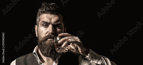 Rich man with a holding glass whiskey. Attractive man with a whiskey. Stylish handsome male in suit drink from glass brandy, cognac. Portrait of a handsome bearded in elegant tuxedo, drink cognac.
