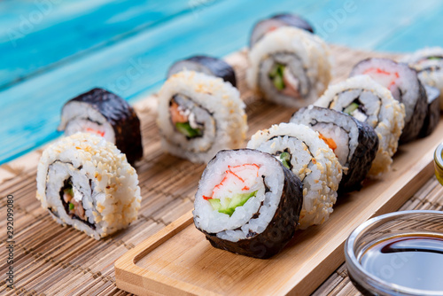 Sushi Rolls in a Row with Salmon, Rice and cucumber on Blue Wood background. White and Black Sushi, Sushi Rolls on Seaweed. Closeup of Delicious Japanese food with Sushi Roll