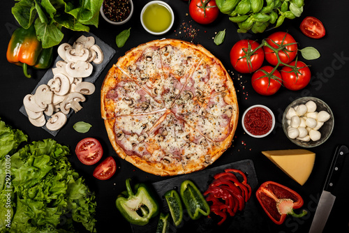 Homemade pizza ready to eat with raw ingredients. Top view on a black background.