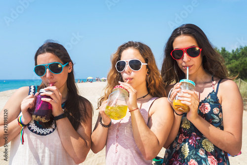 group of happy young women or female friends toasting non alcoholic drinks on summer beach