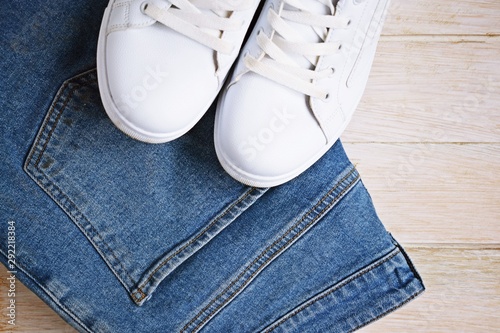 White sneakers and blue jeans on a wooden background.