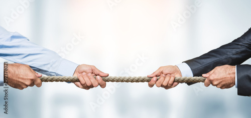Tug of war, two businessman pulling a rope in opposite directions over defocused background with copy space