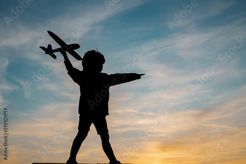 Silhouette of child with airplane in sunlight rays. Concept of dreams and travels. Dreams of flying planes.