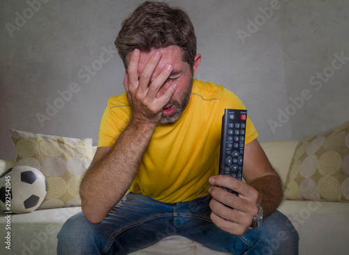 dejected and frustrated man watching European football game on TV sitting at living room couch alone feeling sad and unhappy with his team losing