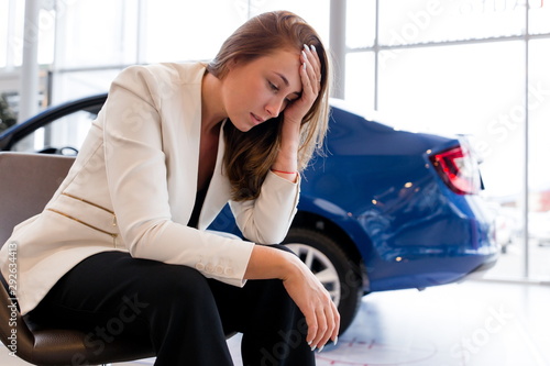 Businesswoman sitting on a chair holding his head from the problems on the background of the car. Confiscation of the car for tax evasion