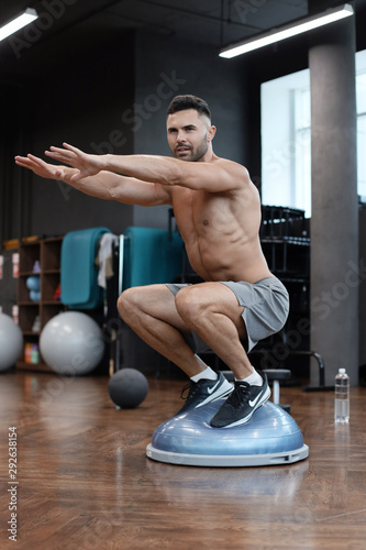 Fit athlete performing exercise on gymnastic hemisphere bosu ball in gym.