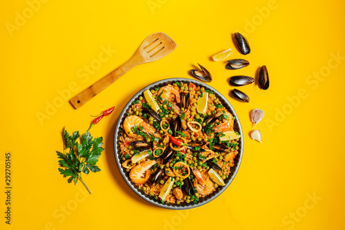 pan with spanish paella with seafood on a yellow background, top view
