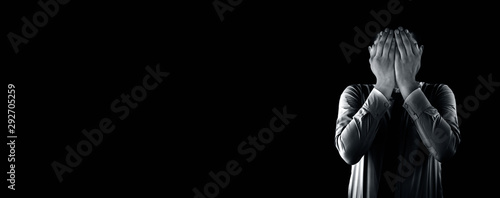 Embarrassed business employee worker wearing a corporate blue shirt with black necktie isolated on black background covering his face with his hands. Wide-angle shot.