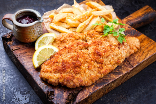 Frittiertes Wiener Schnitzel vom Kalb von der Oberschale mit Pommes Frites und Zitrone als closeup auf einem rustikalen alten Schneidebrett