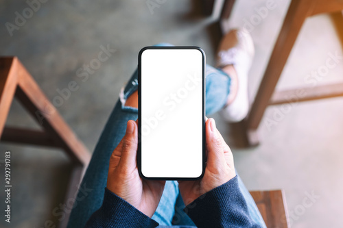 Top view mockup image of a woman holding black mobile phone with blank white screen while sitting in cafe