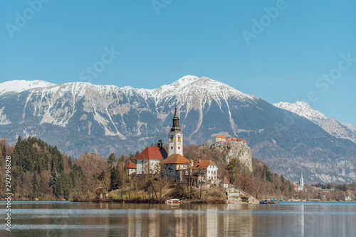 Beautiful view of the island of Bled with its church, in Slovenia, the castle of Bled, and the snow-capped mountains in the background, on a beautiful blue day, without clouds.