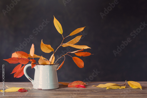 autumn leaves in jug on wooden table on dark background