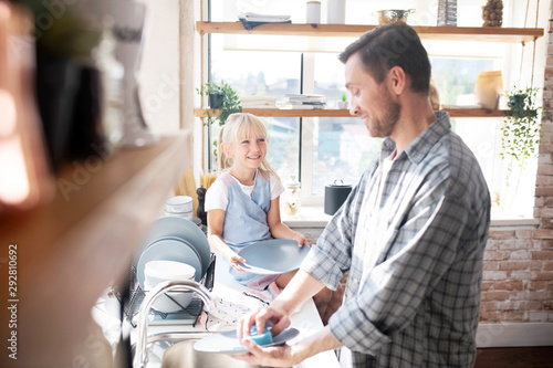 Daughter smiling and talking to daddy washing the dishes