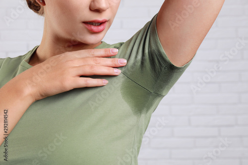 Young woman with sweat stain on her clothes against brick wall, closeup. Using deodorant