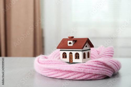 Wooden house model and scarf on grey table indoors. Heating efficiency