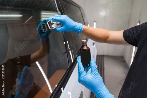 The process of applying a nano-ceramic coating for hydrophobic effect on the car's windows by a male worker with a sponge and