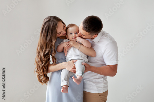 Happy young family. Beautiful Mother and father kissing their baby . Parents, Portrait of Mom, dad and smiling child on hands isolated over white background.