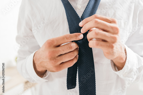 partial view of man in white shirt tying tie