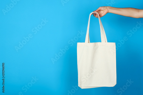 Female hand holding white cotton eco bag on blue background