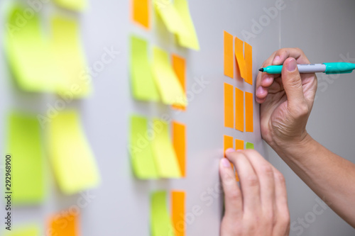 IT worker tracking his tasks on kanban board. Using task control of agile development methodology. Man attaching sticky note to scrum task board in the office