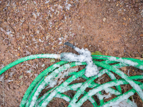 Green garden hose with nozzle sprinkled with snow and ice crystals.