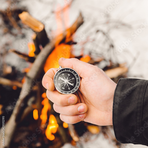 A man holds a compass by the burning bonfire in winter. Concept hike, walk, journey