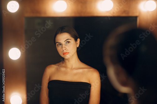 Beautiful young woman doing makeup near the mirror with lamps