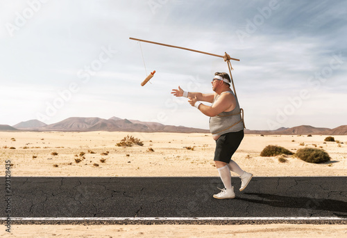 Funny overweight man chasing the hot dog on the stick through the empty road with copy space