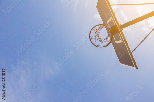 Bottom view on a basketball backboard and a hoop on a sports field in the fresh air in the rays and light of the bright sun against a blue sky. Copyspace on the left. Basketball ring and clear sky.