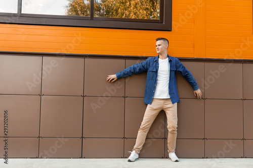 Young man wearing in a blue denim jacket and beige pants stands against the wall. Copyspace.