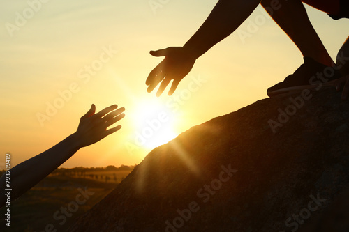 Hiker helping friend outdoors at sunset. Help and support concept