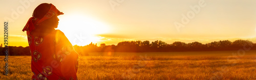 African woman in traditional clothes in field of crops at sunset or sunrise panorama