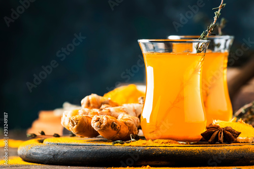 Healthy vegan turmeric golden tea with honey in glass cup on wooden tray. Herbal healing spicy tea
