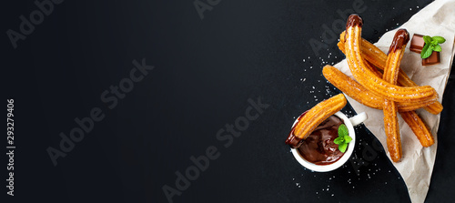 Churros with a cup of hot chocolate on black background. top view. Churro sticks closeup.