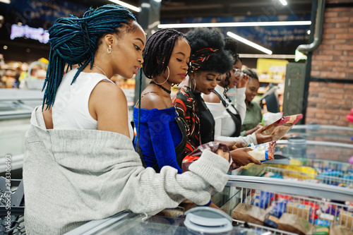 Group of african womans with shopping carts near refrigerator choose packs of dumplings in the supermarket.