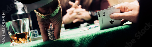 panoramic shot of man touching playing cards and poker chips near player
