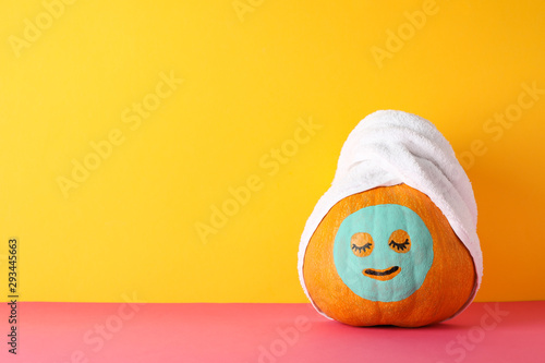 Pumpkin with facial mask and towel against yellow background, copy space
