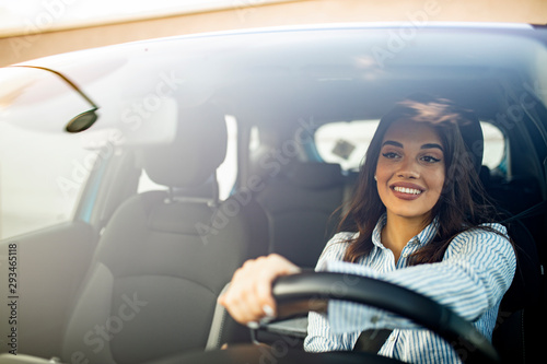 Beautiful young happy smiling woman driving her new car at sunset. Woman in car. Close up portrait of pleasant looking female with glad positive expression, woman in casual wear driving a car