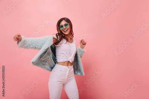 Lovely slim girl posing with sincere smile. Pretty long-haired female model dancing with hands up on pink background.