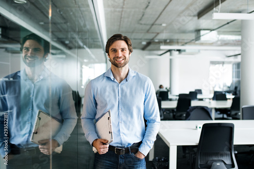 Portrait of young businessman standing in an office, looking at camera.